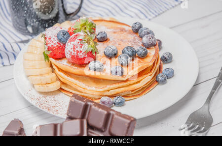 Gesundes Frühstück, Kaffee und leckere hausgemachte Pfannkuchen mit frischen Beeren und Bananen, auf weißer Tisch. Stockfoto