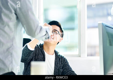 Zwei asiatische junge Geschäftsleute bumping Fäuste Erfolg feiern im Büro. Stockfoto