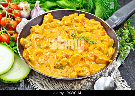 Türkei Fleisch Gulasch mit Tomaten, Zucchini, saure Sahne und Thymian in der Pfanne auf Sackleinen, Löffel und Knoblauch auf Holzbrett Hintergrund Stockfoto