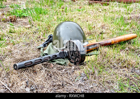 Ein Helm und eine Maschinenpistole aus der Zeit des Großen Vaterländischen Krieges, ein Beutel der schützende Farbe vor dem Hintergrund der Gras Stockfoto
