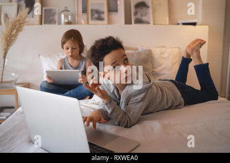 Zwei Kinder, Jungen im Bett der Eltern am Morgen mit Notebook und Tablet-PC. Brüder spielen Computerspiele. Geschwister und Gadgets. Stockfoto