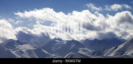 Panoramablick auf die verschneiten Berge in Dunst und sonnendurchfluteten Himmel mit Wolken am Abend. Georgien, Region Gudauri. Kaukasus Berge im Winter. Stockfoto