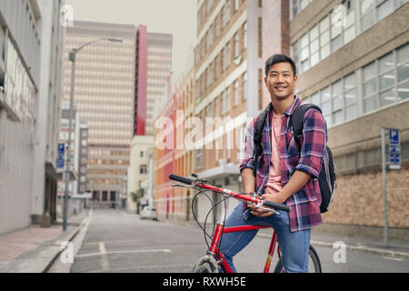 Lächelnden jungen Mann sitzt auf seinem Fahrrad in der Stadt Stockfoto