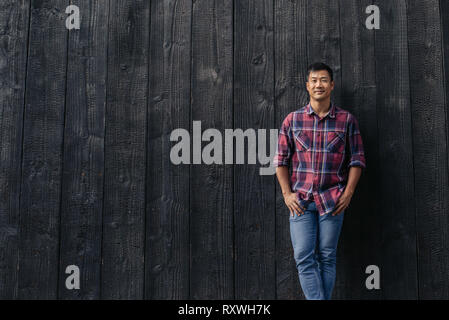Stattliche asiatischer Mann lächelnd, während außerhalb lehnte sich gegen eine Wand. Stockfoto