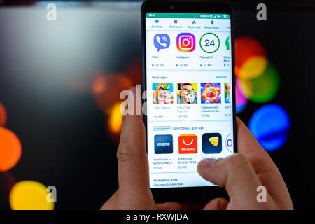 Lemberg, Ukraine - MÄRZ 09, 2019: Der Mann hält das Smartphone in seinen Händen zu schließen und die Anwendung wird geöffnet und Sie können das Google Spiel auf einem verschwommenen Hintergrund Stockfoto