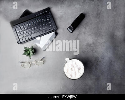 Modernen Arbeitsplatz auf grau Tabelle. Arbeitsplatz Tastatur, Notepad, Kaffee, Gläser, kaktus Stockfoto