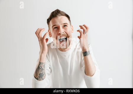 Schreien, Hass, Wut. Weinend emotionale wütenden Mann schreiend auf Grau studio Hintergrund. Emotionale, junges Gesicht. männliche Brustbild. Menschliche Gefühle, Mimik Konzept. Stockfoto