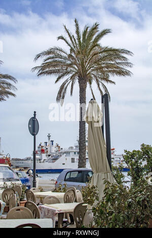 ISOLA LA MADDALENA, Sardinien, Italien - 7. MÄRZ 2019: Fähre in den Hafen über Cafe Tische im Freien mit Palme an einem bewölkten Tag am 7. März 2019 in La M Stockfoto