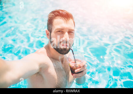 Happy bärtigen Mann, der selfie im Pool. Er trinkt einen Cocktail und entspannend. Stockfoto