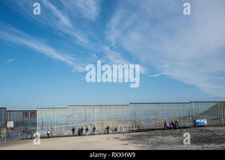 Migranten in Tijuana peer durch den Zaun, auf der anderen Seite der Grenze. Stockfoto