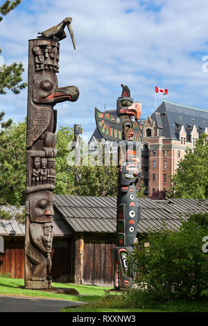 Gruppe von Totems an Thunderbird Park, Royal BC Museum, Victoria, British Columbia, Kanada. Im Hintergrund ist ein Teil der Fairmont Empress Hotel. Stockfoto