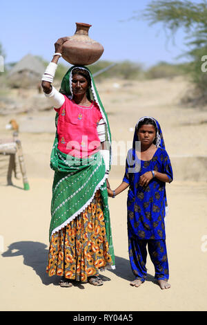 Tharparkar Sindh, Pakistan - März 2019: Dorf der Frau mit Tochter Hand in Buntes Kleid steht in der Wüste mit Wasser Topf auf den Kopf weari Stockfoto