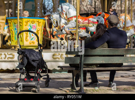 Paar in der Nähe des Karussells auf der Bank sitzen warten auf ein Kind reitet Karussell Stockfoto