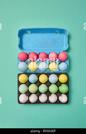 Mehrfarbige helle Ostern Eier in einem blauen und schwarzen Karton auf grünem Hintergrund mit Kopie Raum. Ostern layout für Ihre Ideen. Flach Stockfoto
