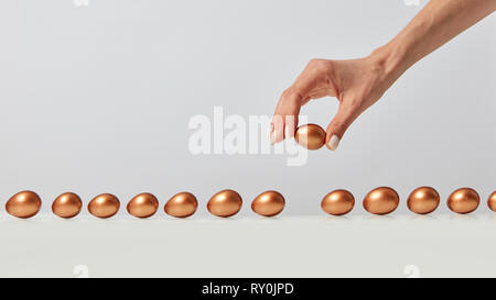 Eine Reihe von goldenen Eiern wird von Hand einer Frau auf einem grauen Hintergrund mit Platz für Text gelegt. Reichtum Konzept Stockfoto