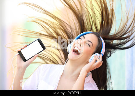 Glückliches Mädchen tanzen Musik hören zeigt leere Smart Phone in einem bunten Straße Stockfoto