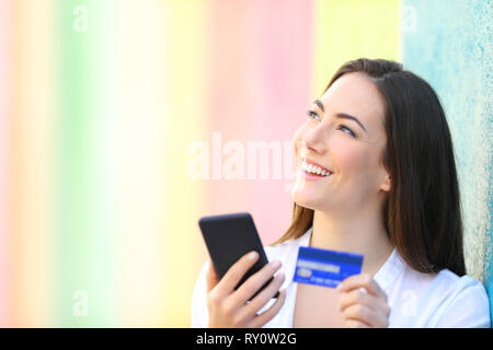 Gerne online shopper Denken zu kaufen was Holding smart phone und Kreditkarte in einem bunten Straße Stockfoto