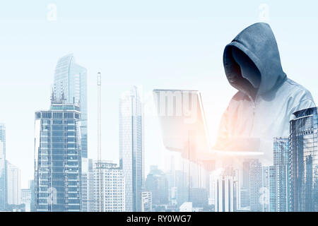Doppelbelichtung Hacker in Schwarz hoodie Holding Laptop und moderne Stadt mit Wolkenkratzern Hintergrund Stockfoto