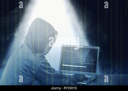Hacker in Schwarz mit Laptop auf dem Schreibtisch zu hacking System mit binären Code hoodie und laden Sie die Malware mit Rauch und Licht von oben über Dunkel Stockfoto