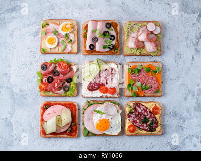 Satz von acht verschiedenen Sandwiches mit Fleisch in quadratische Form. Top View oder flach. Sortiment Fleisch Toast auf grauem Zement Hintergrund. Idee, kreatives Konzept für wurstmacher Stockfoto