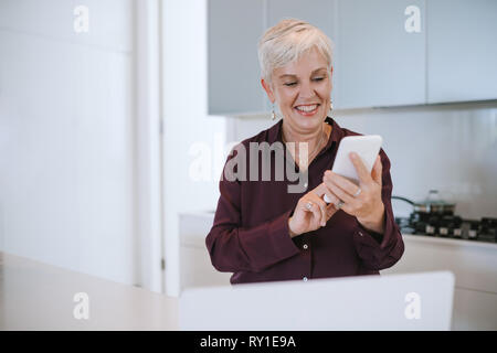 Porträt einer wunderschöne reife Frau lächelnd, mit Ihrem Mobiltelefon, in der Küche Stockfoto