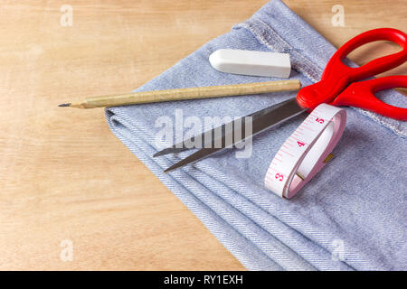 Ausrüstung für Jeans Stoff Schneiden auf braunem Holz Hintergrund. Stockfoto