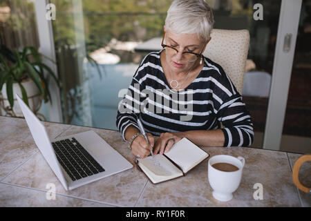 Kreative Prozess, in dem neuen Text. Ältere Frau leben oder Business Coach schreiben Sie Gedanken, Ideen in Copybook und Arbeiten am Laptop, Nahaufnahme Stockfoto