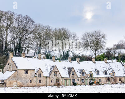 Arlington Row bedeckt mit Schnee unter einem blassen winterlichen Himmel in Bibury, Gloucestershire, Großbritannien Stockfoto