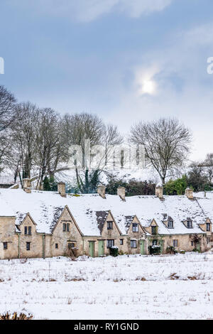 Arlington Row bedeckt mit Schnee unter einem blassen winterlichen Himmel in Bibury, Gloucestershire, Großbritannien Stockfoto