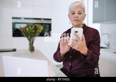 Porträt einer schönen reife Frau, mit Ihrem Mobiltelefon, in der Küche mit Laptop Stockfoto