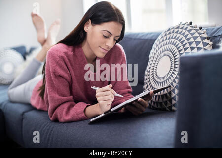 Junge Frau entspannt auf einem Sofa zu Hause Schreiben im Journal Stockfoto