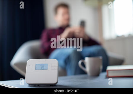 Man Controlling Zentralheizung Smart Meter über App auf dem Mobiltelefon Stockfoto