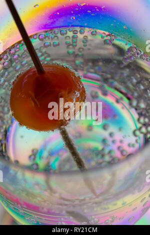 Interessante stress Patterns in Kunststoff Wein Glas mit roter Kirsche auf Cocktail stick in Gin Tonic trinken, die sonderbare Erscheinung gesehen Stockfoto