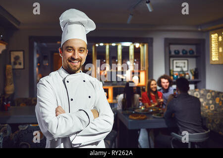 Ein männlicher Cook ist lächelnd vor dem Hintergrund der ein Restaurant. Stockfoto