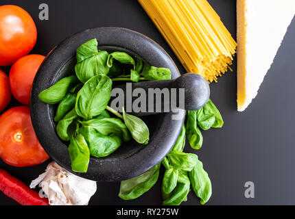 Vorbereitung italienische Pasta mit frischem Basilikum in Mörtel, Tomaten, Knoblauch, Pfeffer und Parmesan auf dunklen Küche Zähler Stockfoto