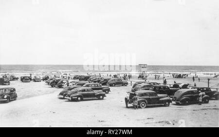 Horizontale schwarze und weiße Foto von Menschen und Autos am Strand in den späten 1940er Jahren. Stockfoto