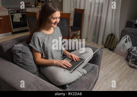 Junge Frau kommuniziert in sozialen Netzwerken mit Laptop, Mädchen zu Hause sitzen im Stuhl mit Laptop Stockfoto