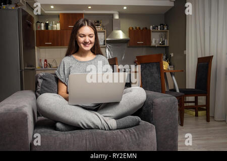 Junge Frau kommuniziert in sozialen Netzwerken mit Laptop, Mädchen zu Hause sitzen im Stuhl mit Laptop Stockfoto