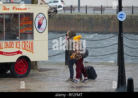 Eine Frau und ein junges Mädchen in einem Eis van, während Sie zu Fuß auf einen sehr nassen und windigen Tag in Liverpool, Großbritannien. Stockfoto