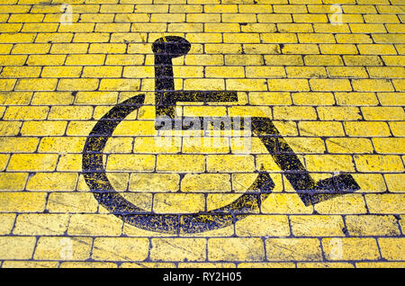 Rollstuhl Symbol in Schwarz auf Gelb Pflaster auf einen Parkplatz für behinderte Besucher Stockfoto