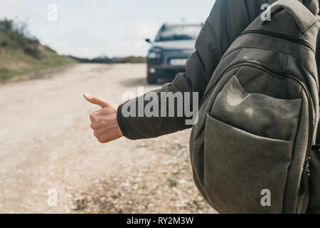 Nahaufnahme eines Mannes Wanderer mit Rucksack trampen. Er hob den Finger auf und versucht, das Auto seine Reise fortsetzen zu stoppen. Stockfoto