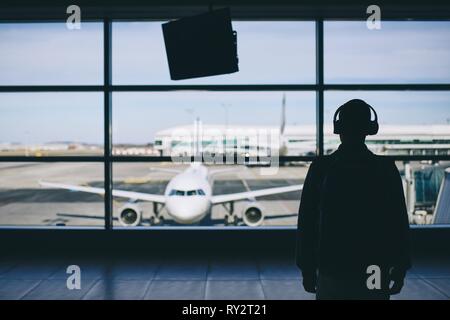 Passagier mit Kopfhörern. Junger Mann zu Fuß durch Flughafen Flugzeug. Stockfoto