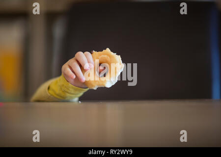 Kleines Kind Holding halb gegessen Donut über einem Esstisch Stockfoto