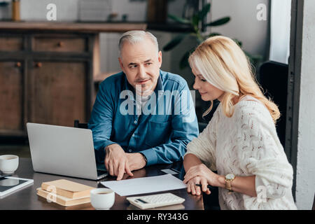 Schöner Mann zeigte mit dem Finger auf leeres Papier, während attraktive blonde Frau suchen Stockfoto