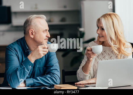 Freundliche Paar hält Cups mit Getränke und an jedem anderen zu Hause suchen Stockfoto