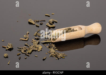 Viele Stücke von trockenen Grüner Tee mit Holz- Schaufel auf schwarzem Glas Stockfoto