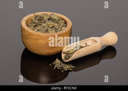 Viele Stücke von trockenen grünen Tee in eine Schaufel mit Houten auf schwarzem Glas Stockfoto