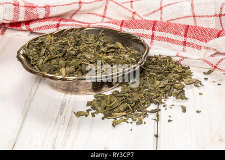 Viele Stücke von trockenen grünen Tee in Altes Eisen Schüssel auf weißem Holz Stockfoto