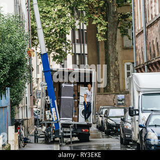 Straßburg, Frankreich - 12.September 2017: Square Image der jungen männlichen Arbeitnehmer in das Fahrzeug warten auf den hydraulischen Aufzug Boom ein weiteres Paket während Home Umzug zu liefern Stockfoto