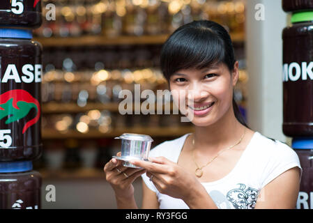 Eine asiatische Frau lächelnd mit einem vietnamesischen Kaffee - heiße Milch Kaffee mit Kondensmilch in Vietnam Stil. Traditionelle vietnamesische Trinken Stockfoto